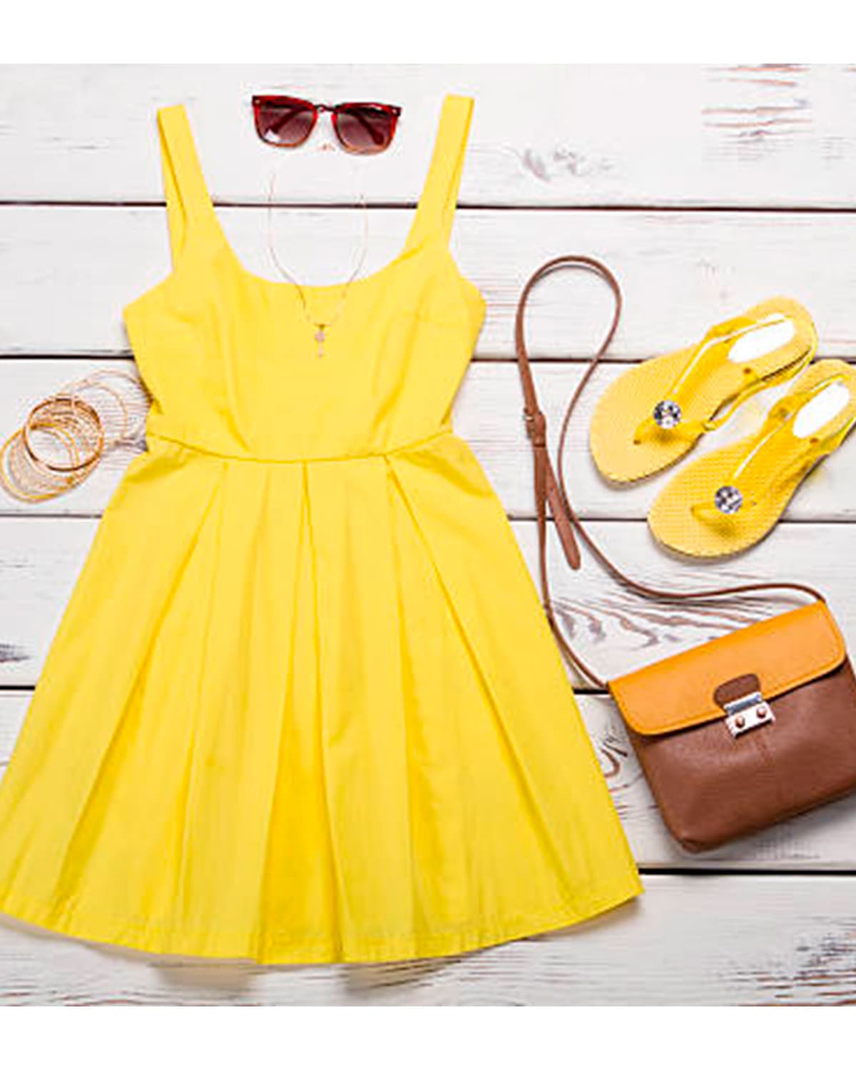 Vestido amarillo junto a cartera, sandalias y anteojos.